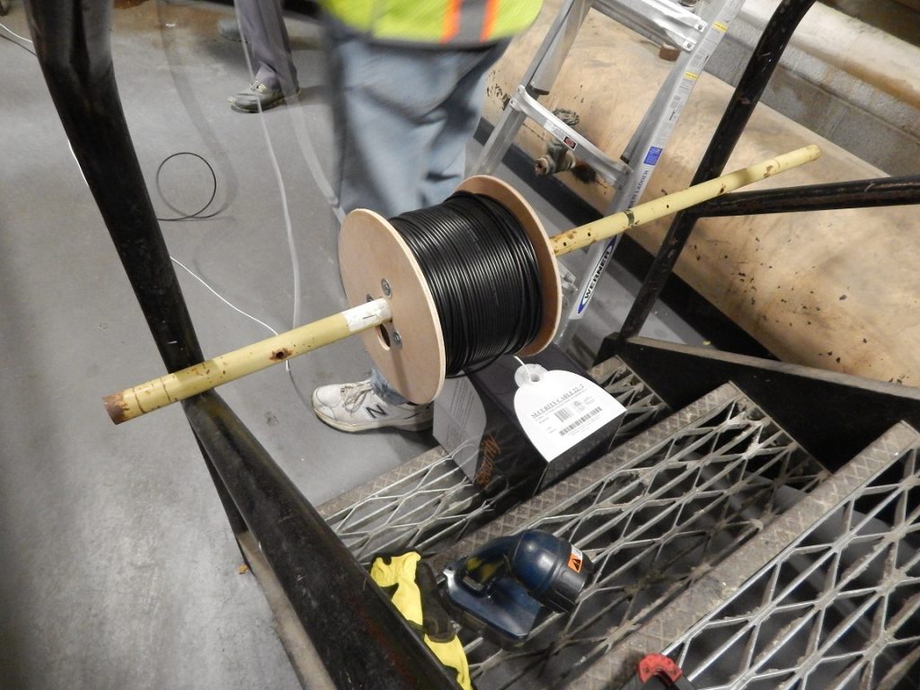 Use of broomstick to spool out fiber cable from roll.